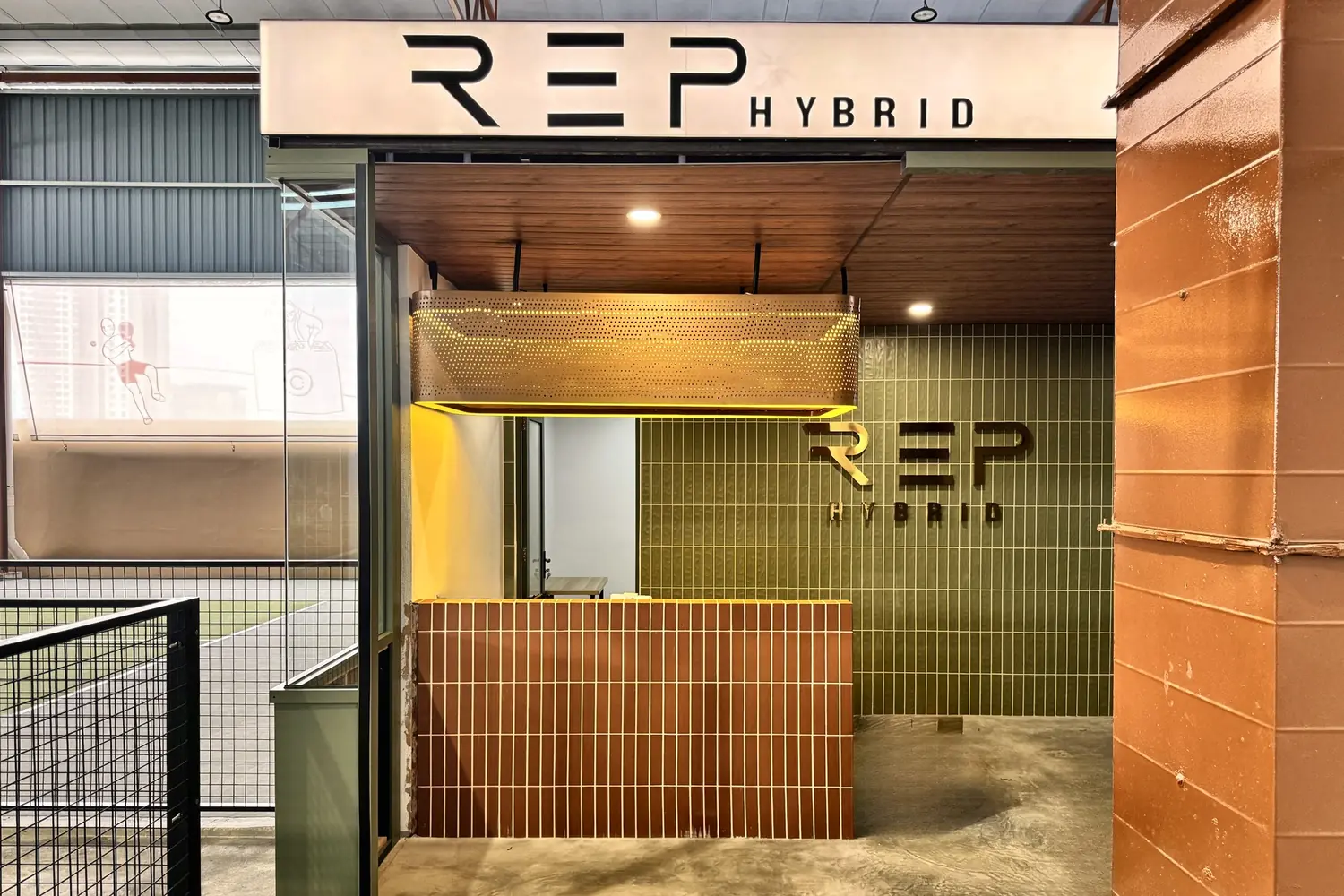 The REP HYBRID front desk: a terracotta tiled counter under a lit perforated canopy, green tiles and the REP logo behind